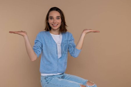 Photo for Cheerful satisfied woman in casual clothing spreading hands copy space isolated over beige background. - Royalty Free Image