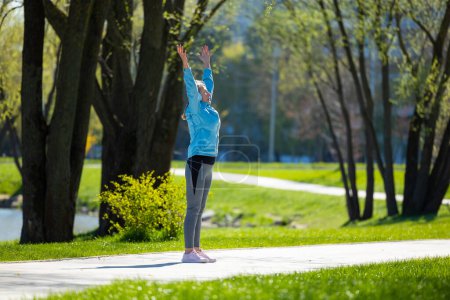 Photo for Sun salutation. Woman standing on the park road with her arms up - Royalty Free Image