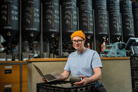 Photo for Handsome barista working in coffee shop, accepts new product, checks the amount of coffee, using notebook - Royalty Free Image