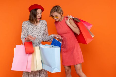 Photo for Adult women friends looking inside shopping bags isolated over orange background. - Royalty Free Image