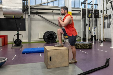 Téléchargez les photos : Homme sportif en vêtements de sport faire intensifier l'entraînement avec une boîte en bois dans la salle de gym Crossfit. - en image libre de droit