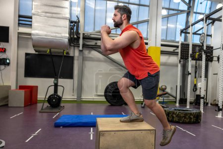 Téléchargez les photos : Homme sportif en vêtements de sport faire intensifier l'entraînement avec une boîte en bois dans la salle de gym Crossfit. - en image libre de droit