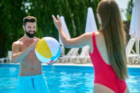 Téléchargez les photos : Heureux couple attrayant s'amuser dans la piscine avec ballon de plage, profiter du repos actif à la station. - en image libre de droit