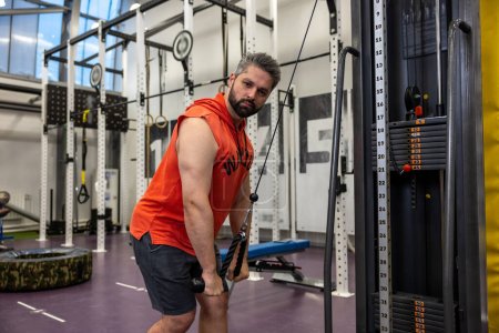 Foto de Hombre deportivo fuerte en tríceps de entrenamiento de ropa deportiva y bíceps en el gimnasio, haciendo empujones de cuerda de cable. - Imagen libre de derechos
