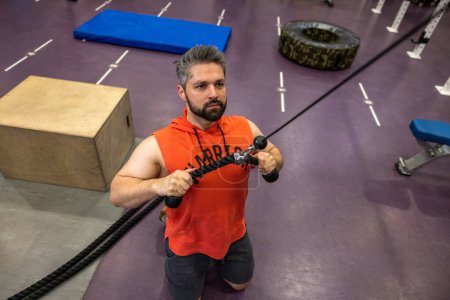 Téléchargez les photos : Homme sportif fort en triceps et biceps d'entraînement de vêtements de sport à la salle de gym, faisant des poussées de câble debout sur les genoux. - en image libre de droit