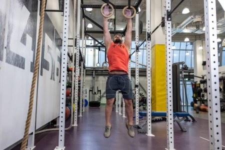 Foto de Adulto barbudo en forma hombre tirando de anillos de gimnasia en el gimnasio, el entrenamiento, el entrenamiento de sus bíceps y tríceps. - Imagen libre de derechos