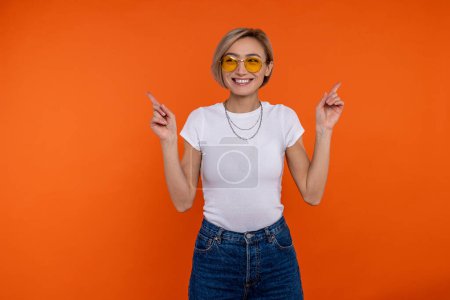 Photo for Adorable woman in white t shirt and jeans pointing at both hands at empty space for promotion isolated over orange background. - Royalty Free Image