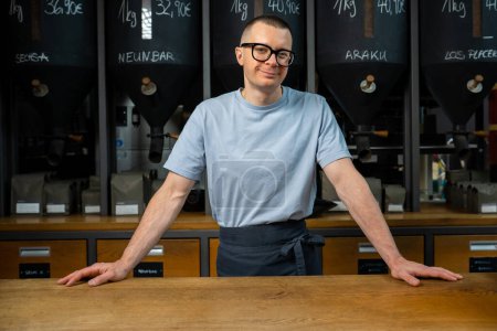 Photo for Barista bartender wearing apron and glasses standing near counter of his cafe with big variety of coffee. - Royalty Free Image