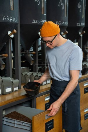 Foto de Cafetera caucásica con gorro sombrero y vasos de trabajo en la tienda de café tostado. - Imagen libre de derechos