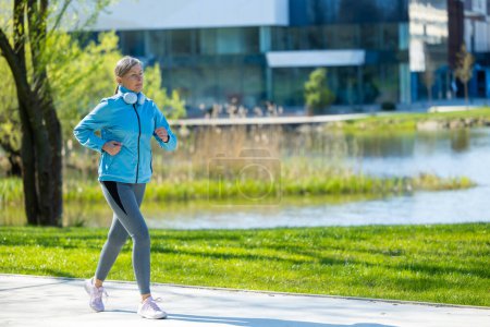 Téléchargez les photos : Du jogging. Femme mature jogging dans le parc et à la recherche concentrée - en image libre de droit