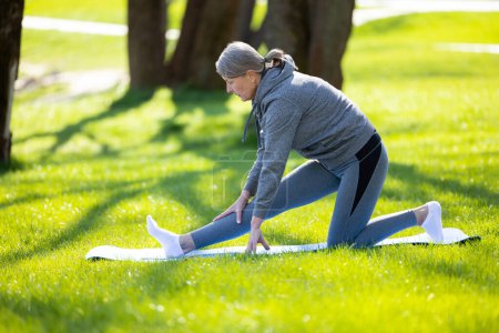 Téléchargez les photos : Bonjour, yoga. Femme en vêtements de sport gris faisant du yoga dans le parc - en image libre de droit