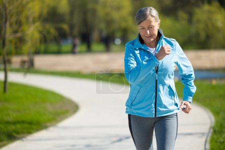 Photo for Running in the park. Mature good-looking woman running in the park and looking contened - Royalty Free Image