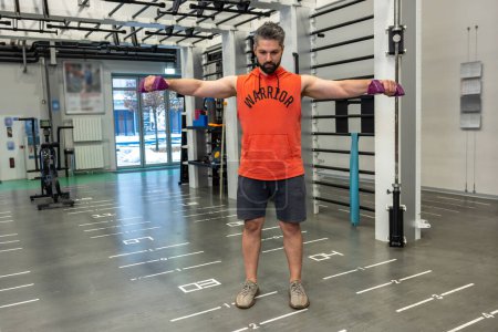Foto de Adulto barbudo hombre deportivo trabajando en sus bíceps, levantando pesas brazos entrenamiento en el gimnasio. - Imagen libre de derechos