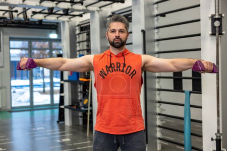 Téléchargez les photos : Homme athlétique avec barbe travaillant sur ses biceps et triceps soulevant haltères bras d'entraînement dans la salle de gym. - en image libre de droit
