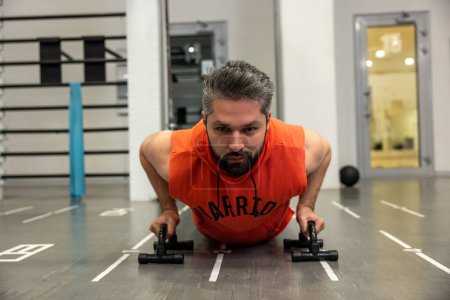 Foto de Entrenamiento intensivo en gimnasio moderno, hombre de pie en posición de tablón o haciendo ejercicios en soportes push-up. - Imagen libre de derechos