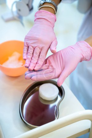 Foto de Mujer cosmetóloga irreconocible en guantes de goma rosa tomando crema preparándose para los procedimientos de belleza. - Imagen libre de derechos