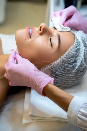 Téléchargez les photos : Médecin esthéticienne méconnaissable faisant des procédures de nettoyage du visage à la femme dans la clinique de cosmétologie. - en image libre de droit