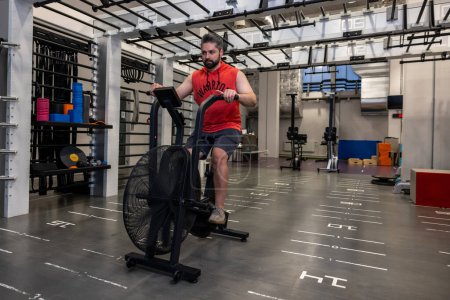 Foto de Hombre atlético adulto en ropa deportiva haciendo ciclismo en bicicletas estáticas en el gimnasio. - Imagen libre de derechos