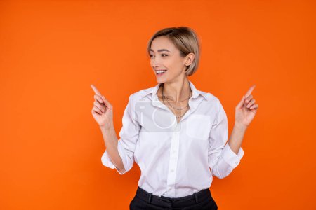 Foto de Mujer alegre con camisa blanca de estilo oficial apuntando a ambos lados para copiar el espacio aislado sobre fondo naranja. - Imagen libre de derechos