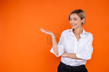 Photo for Satisfied woman wearing white official style shirt showing empty space on palm isolated over orange background. - Royalty Free Image