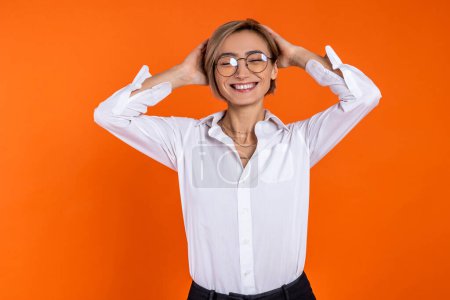 Photo for Satisfied woman wearing white official style shirt standing smiling with raised arms isolated over orange background. - Royalty Free Image