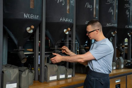 Téléchargez les photos : Travailleur de café dans des verres et tablier debout au comptoir versant des grains de café. - en image libre de droit