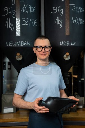 Photo for Coffee shop worker in glasses and apron standing at counter. - Royalty Free Image