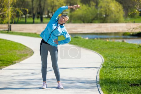 Foto de Estiramiento. Mujer en blusa ropa deportiva haciendo estiramiento en el parque - Imagen libre de derechos