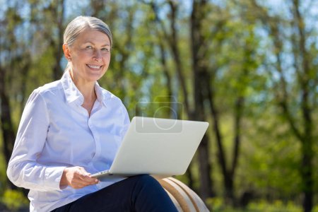 Téléchargez les photos : Je travaille dehors. Femme d'affaires avec ordinateur portable assis sur le banc dans le parc - en image libre de droit