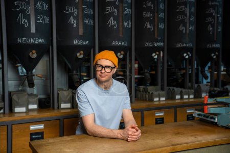 Foto de Cafetera. Profesional hipster barista en gorro sombrero y vasos de pie en el mostrador de bar en la cafetería. - Imagen libre de derechos