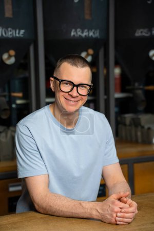 Foto de Amistoso camarero hipster con gafas en el interior de la cafetería moderna con gran variedad de granos de café. - Imagen libre de derechos