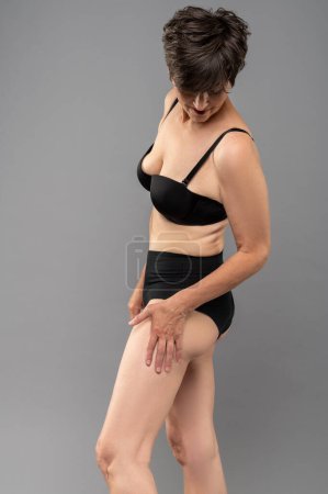 Foto de Envejecimiento. Mujer en lencería negra escudriñando sus piernas - Imagen libre de derechos