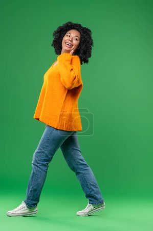Téléchargez les photos : Heureux. Jeune femme aux cheveux bouclés en orange sur fond vert - en image libre de droit