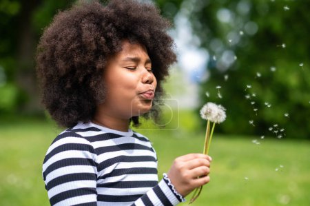 Photo for Dandelion. Curly-haired kid blowing on a dandelion - Royalty Free Image