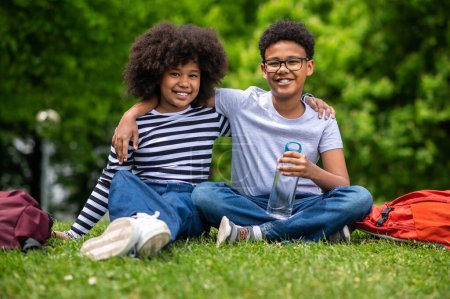 Téléchargez les photos : L'amitié. Deux enfants afro-américains assis sur l'herbe dans le parc - en image libre de droit