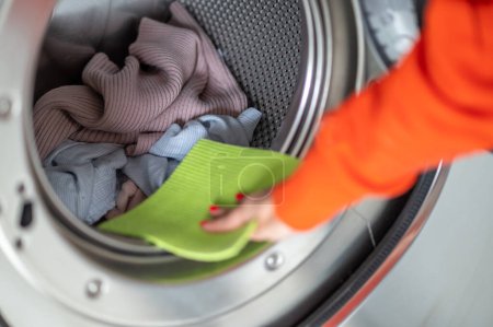 Téléchargez les photos : Blanchisserie publique. Femme méconnaissable lavant des vêtements sales, nettoyant la machine à laver avec chiffon dans la buanderie. - en image libre de droit