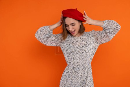 Téléchargez les photos : Femme adulte frustrée portant une robe élégante et un béret rouge bras levés criant debout isolé sur fond orange. - en image libre de droit