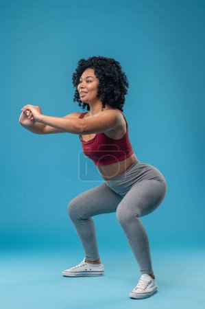 Photo for Excercising. Curly-haired young woman excercising and doing squats - Royalty Free Image