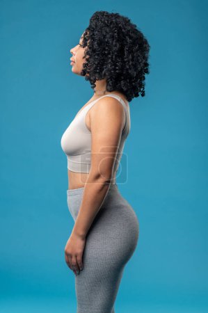 Photo for Sporty woman. Curly-haired woman standing on a blue background - Royalty Free Image