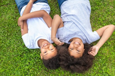 Photo for Top view of cute little boy and girl smiling while lying the grass in park. - Royalty Free Image