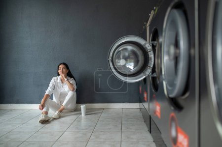 Foto de Joven morena esperando en la lavandería pública. - Imagen libre de derechos