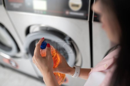 Foto de Mujer irreconocible en lavandería poniendo detergente de limpieza en la lavadora en la lavandería pública. - Imagen libre de derechos