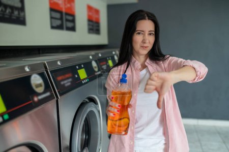 Foto de Mujer morena en lavandería mostrando mal detergente de limpieza, mostrando el pulgar hacia abajo. - Imagen libre de derechos