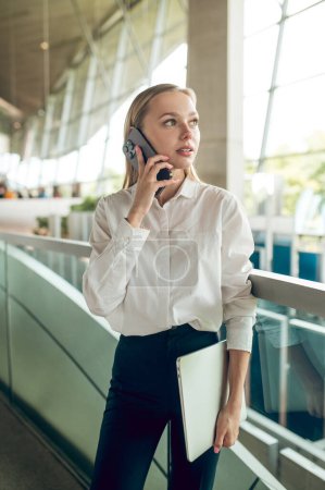 Foto de En una llamada. Rubia joven mujer de negocios que tiene una llamada telefónica - Imagen libre de derechos
