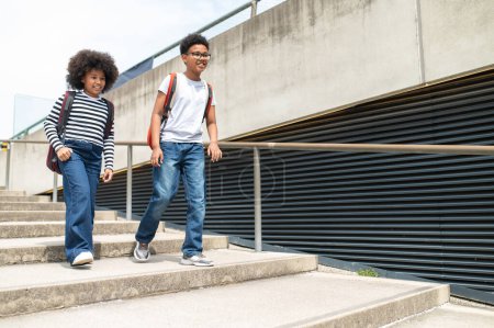Foto de Colegiales activos corriendo en escaleras con mochilas con camisas casuales y jeans caminando divirtiéndose después de la escuela. - Imagen libre de derechos