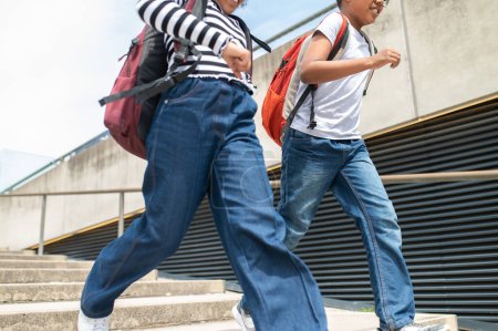 Téléchargez les photos : Écoliers actifs méconnaissables courant dans les escaliers avec des sacs à dos portant des chemises et des jeans décontractés marchant en s'amusant après l'école. - en image libre de droit