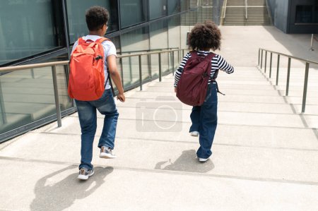 Photo for Back view of active schoolchildren running on stairs with backpacks wearing casual shirts and jeans walking having fun after school. - Royalty Free Image