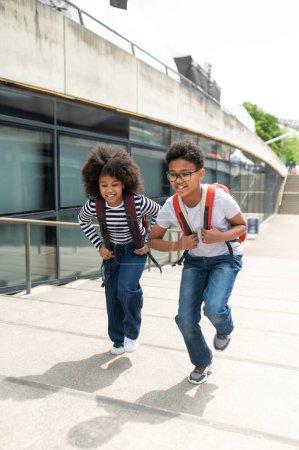 Photo for Happy schoolchildren running on stairs with backpacks wearing casual shirts and jeans walking having fun after school. - Royalty Free Image