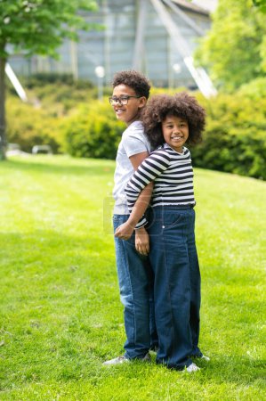 Foto de Dos amigos chico y chica divirtiéndose en el parque de pie espalda con espalda jugando al aire libre durante las vacaciones de verano. - Imagen libre de derechos