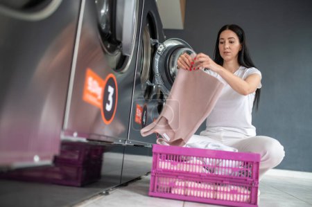 Téléchargez les photos : Femme utilisant une machine à laver qualifiée dans la salle publique pour laver ses draps, une blanchisserie commerciale en libre-service et une machine à sécher dans une salle publique. - en image libre de droit